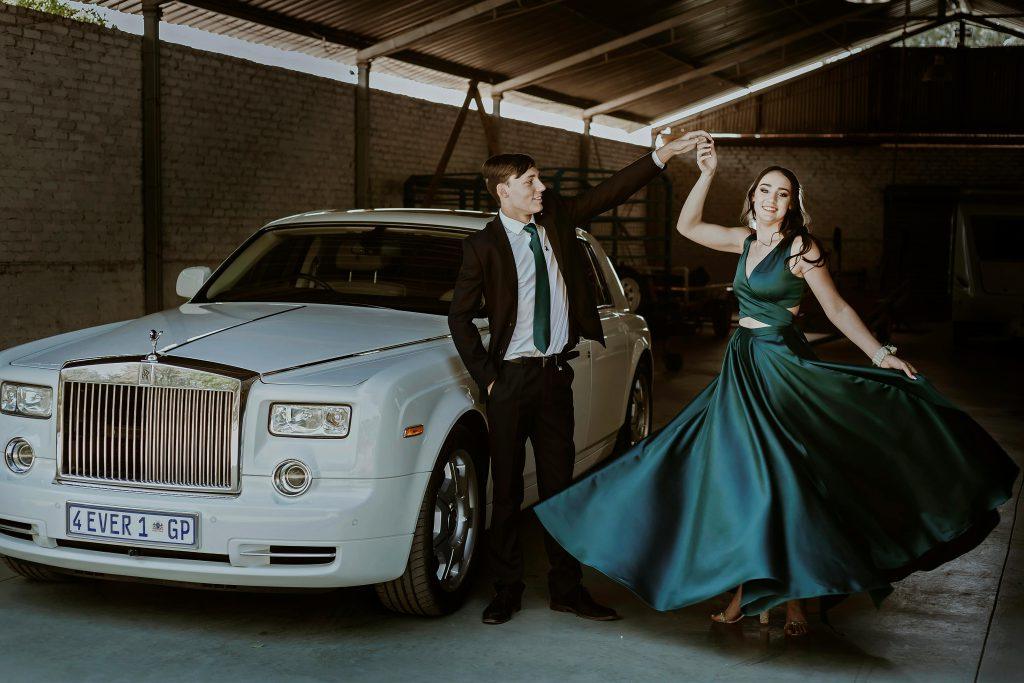 A stylish couple elegantly dancing beside a white Rolls-Royce in a garage setting.