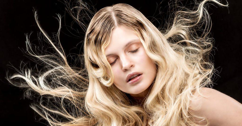 Stylish portrait of a woman with flowing blonde hair and closed eyes on a black background.